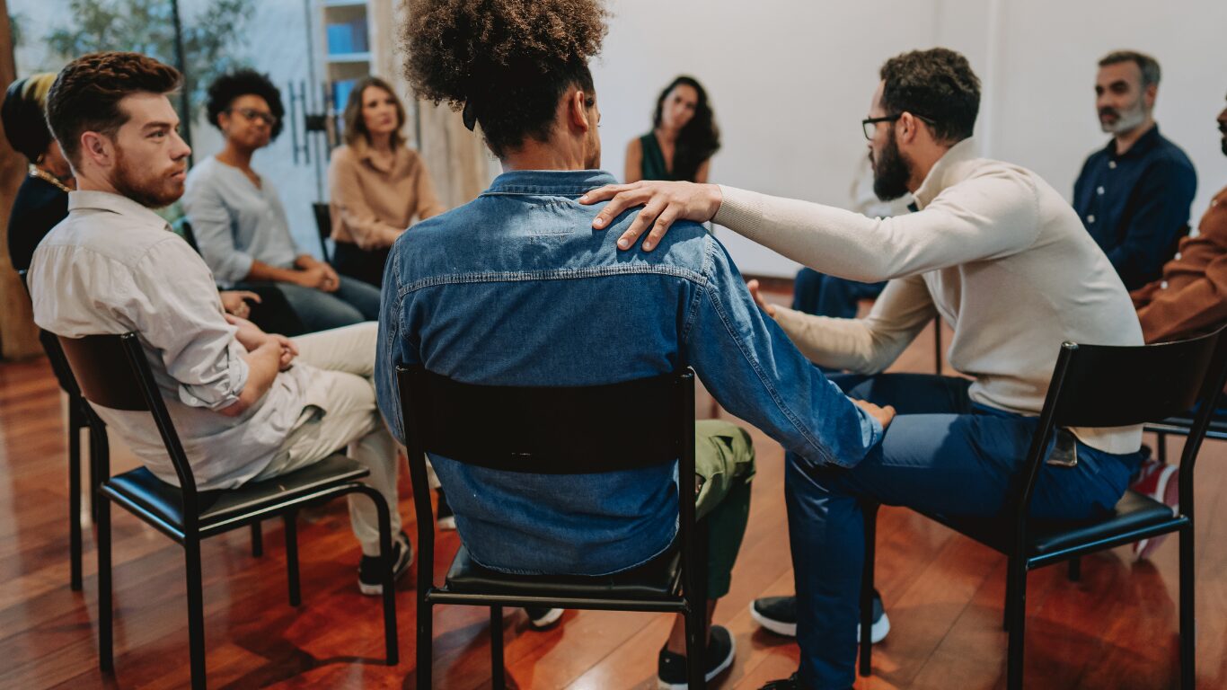 Group therapy session with supportive hand on shoulder