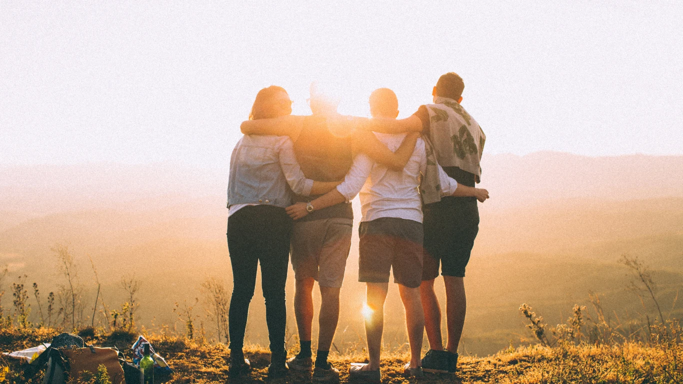 Four friends embracing on hilltop at sunset