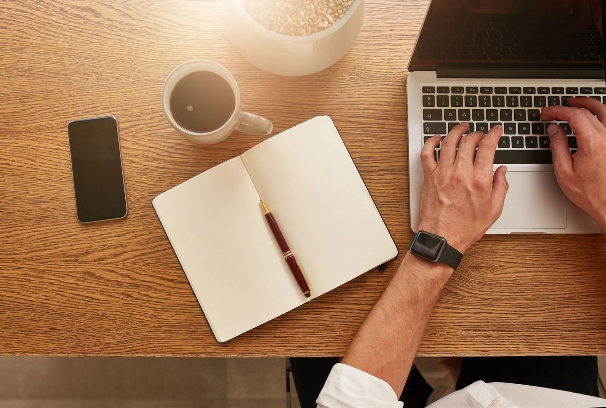 Hands typing on laptop with notebook and coffee